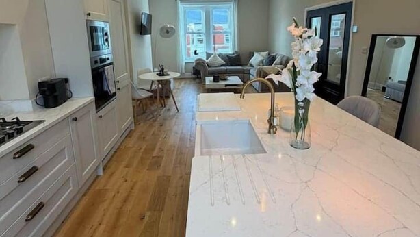 Una cocina moderna con una isla central, armarios blancos y un ventanal amplio.