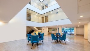 A spacious, multi-level interior with a central seating area featuring blue chairs and tables. - Limewood Signature-Golf Course Extension (Gurugram)
