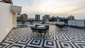 A rooftop terrace with a geometric patterned floor, outdoor seating, and a view of high-rise buildings in the background. - Limewood Signature-Golf Course Extension (Gurugram)
