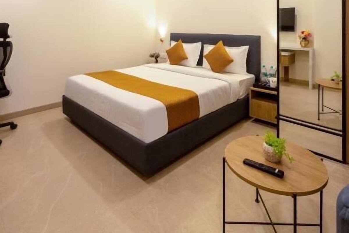 Una habitación de hotel moderna con una cama grande, mesitas de noche, una pequeña mesa redonda y un espejo.
