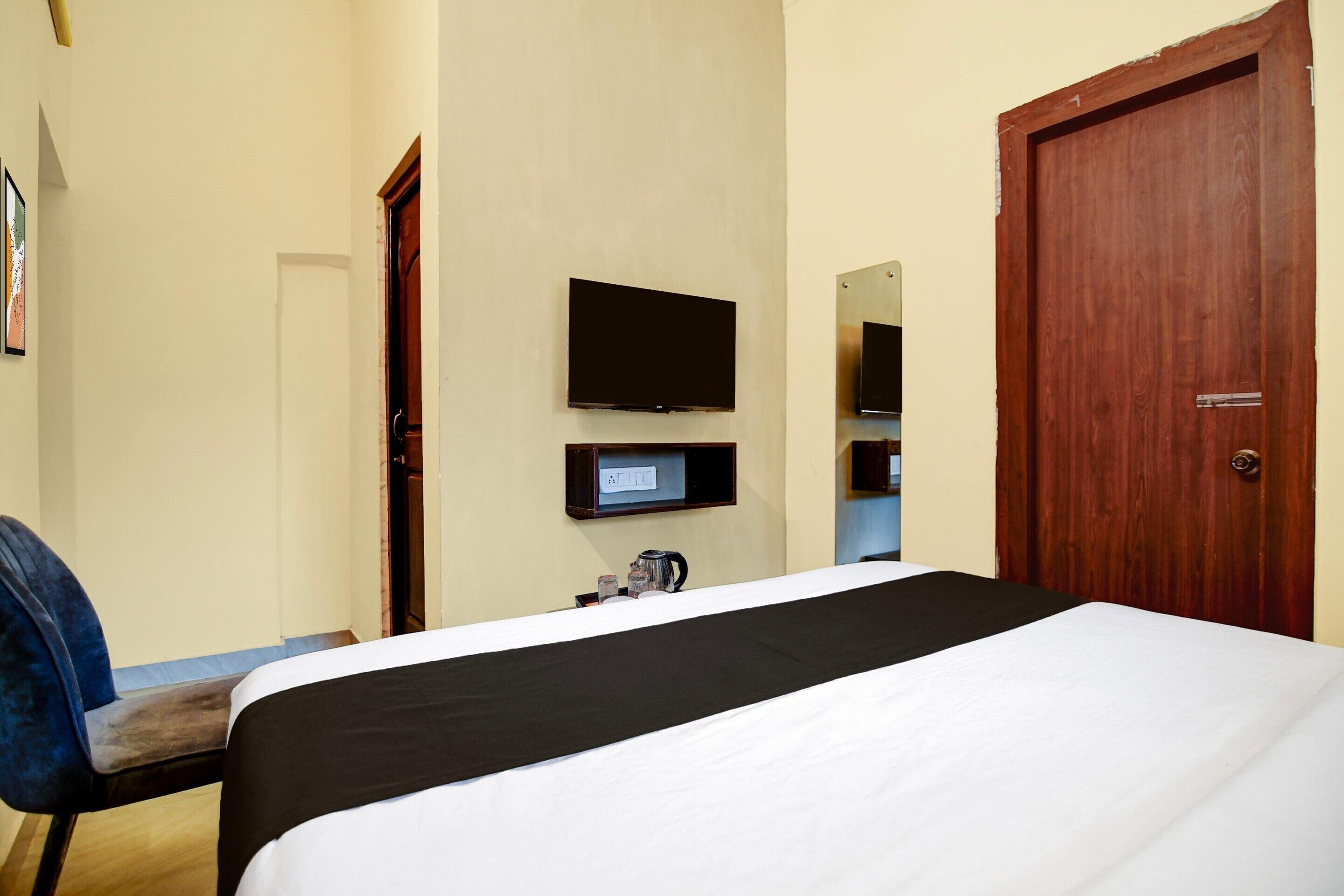 A hotel room with a bed, a television mounted on the wall, a wooden door, and a chair.