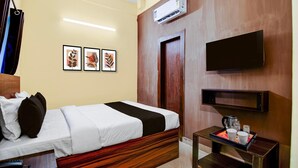Habitación de hotel con una cama, una mesita de noche con cafetera, un televisor de pantalla plana montado en la pared y obras de arte enmarcadas.