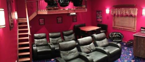A room with a red wall, a black leather couch, a wooden staircase, and a small table with chairs.