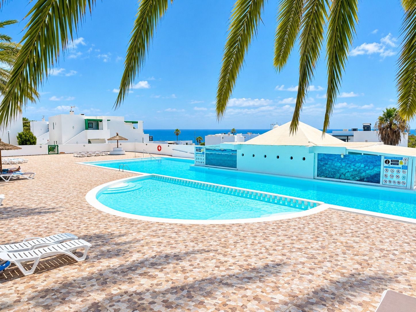 Área de piscina com espreguiçadeiras, piscina e vista para o mar.