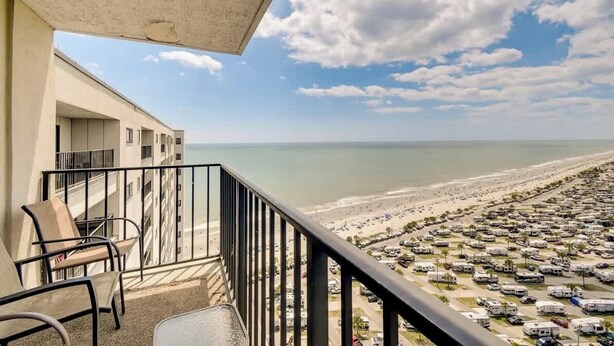 A balcony with chairs overlooking a beach and a parking lot. - Penthouse 2BR, Wi-Fi, SMART TVs, Amazing Views! (Myrtle Beach)
