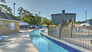 A swimming pool with a blue tiled edge, a fenced area with lounge chairs, and a building in the background. - Penthouse 2BR, Wi-Fi, SMART TVs, Amazing Views! (Myrtle Beach)