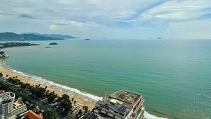 Un paisaje costero con playa, un edificio grande con terraza en la azotea y montañas lejanas.