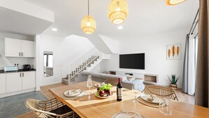 Ett modernt kök med vita skåp, ett träbord med plats för fyra personer och en trappa som leder upp till ett vardagsrum med en platt-TV.