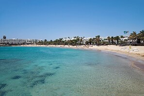 Ein Strand mit klarem türkisblauem Wasser, Palmen und einer Reihe weißer Gebäude mit Balkonen.