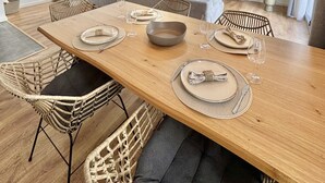 Ett rymligt vardagsrum med ett matbord i trä som är dukat för sex personer, omgivet av stolar i rotting. En trappa med vita räcken leder upp till en övre våning.