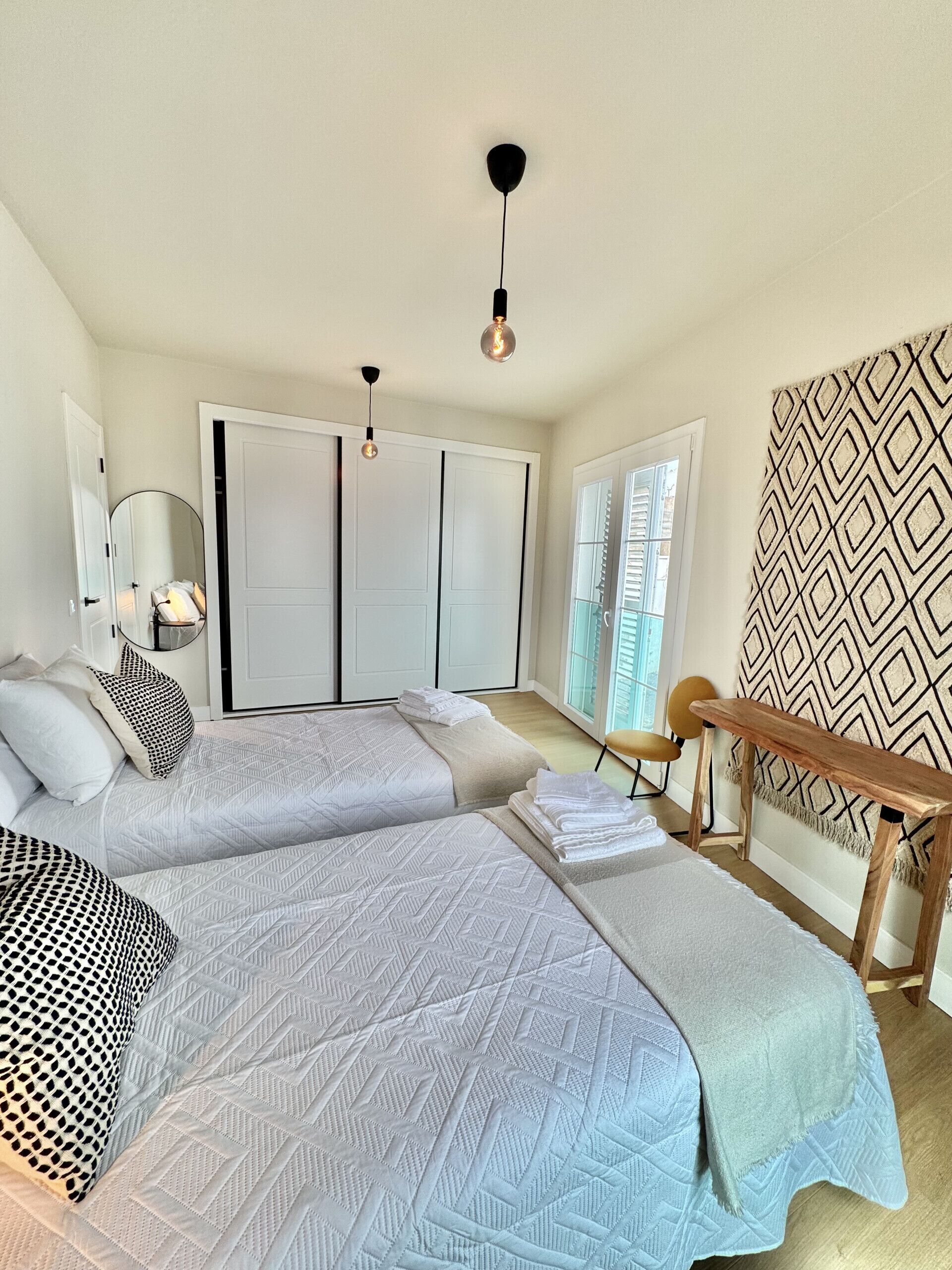 Une chambre avec deux lits, un banc en bois, un mur à motifs et une armoire.