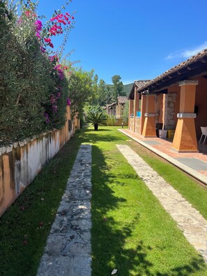 A pathway flanked by greenery and a building with stone pillars and tiled roofs. - Vacation Home (Sardegna)