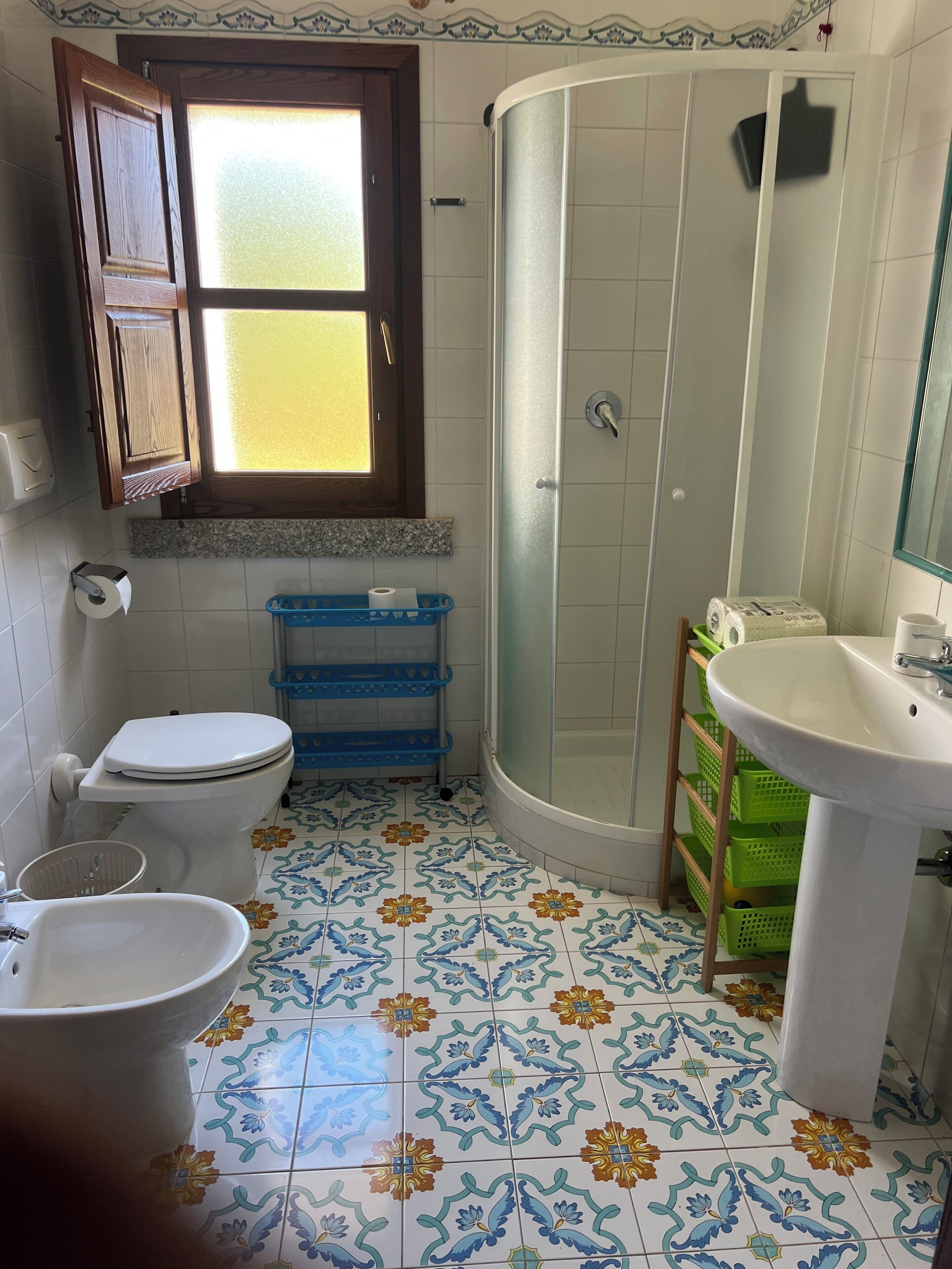 A bathroom with a toilet, sink, shower, and a window with a wooden frame.