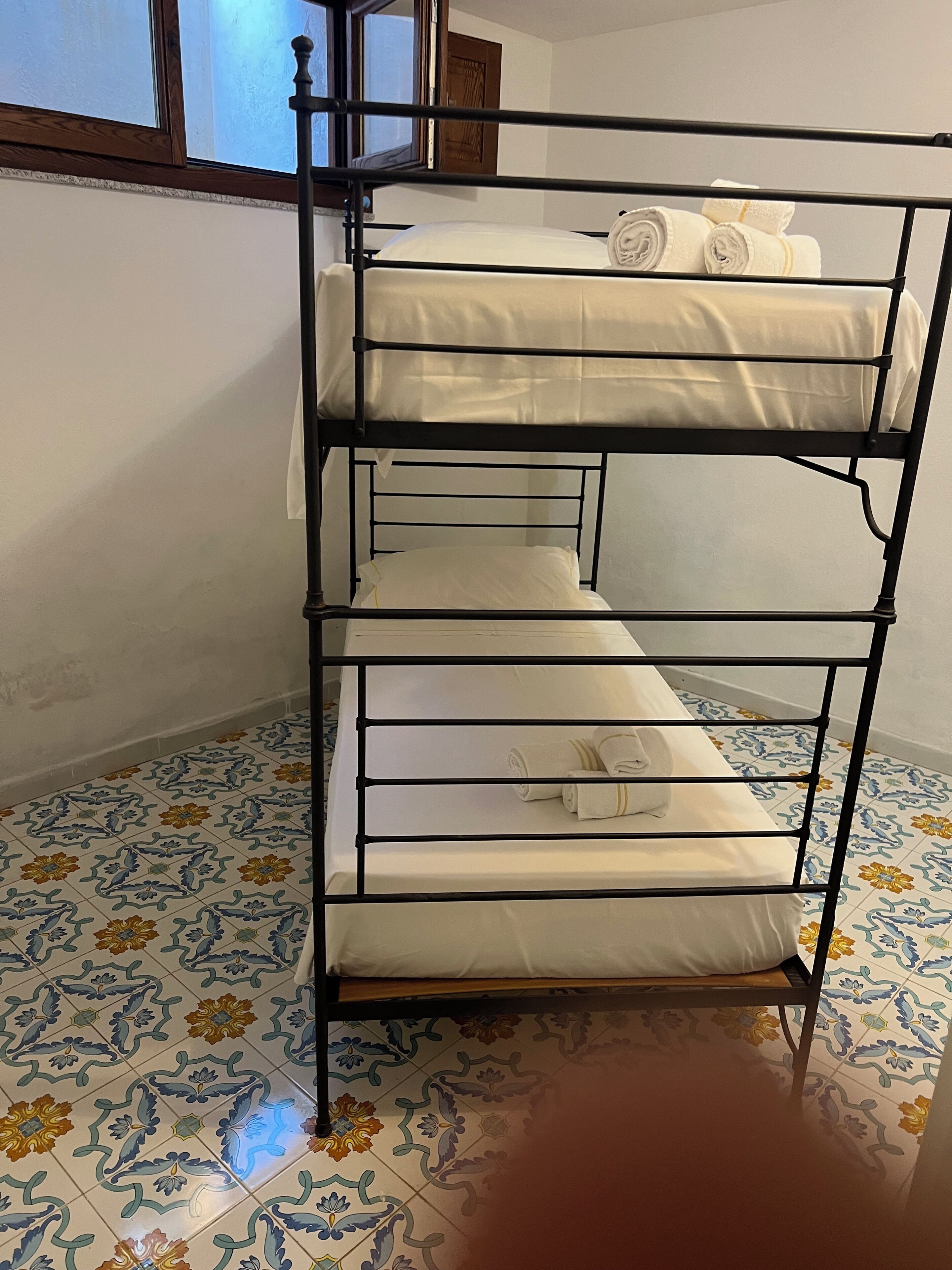 A bunk bed with white bedding and towels, a window with a wooden frame, and patterned floor tiles.