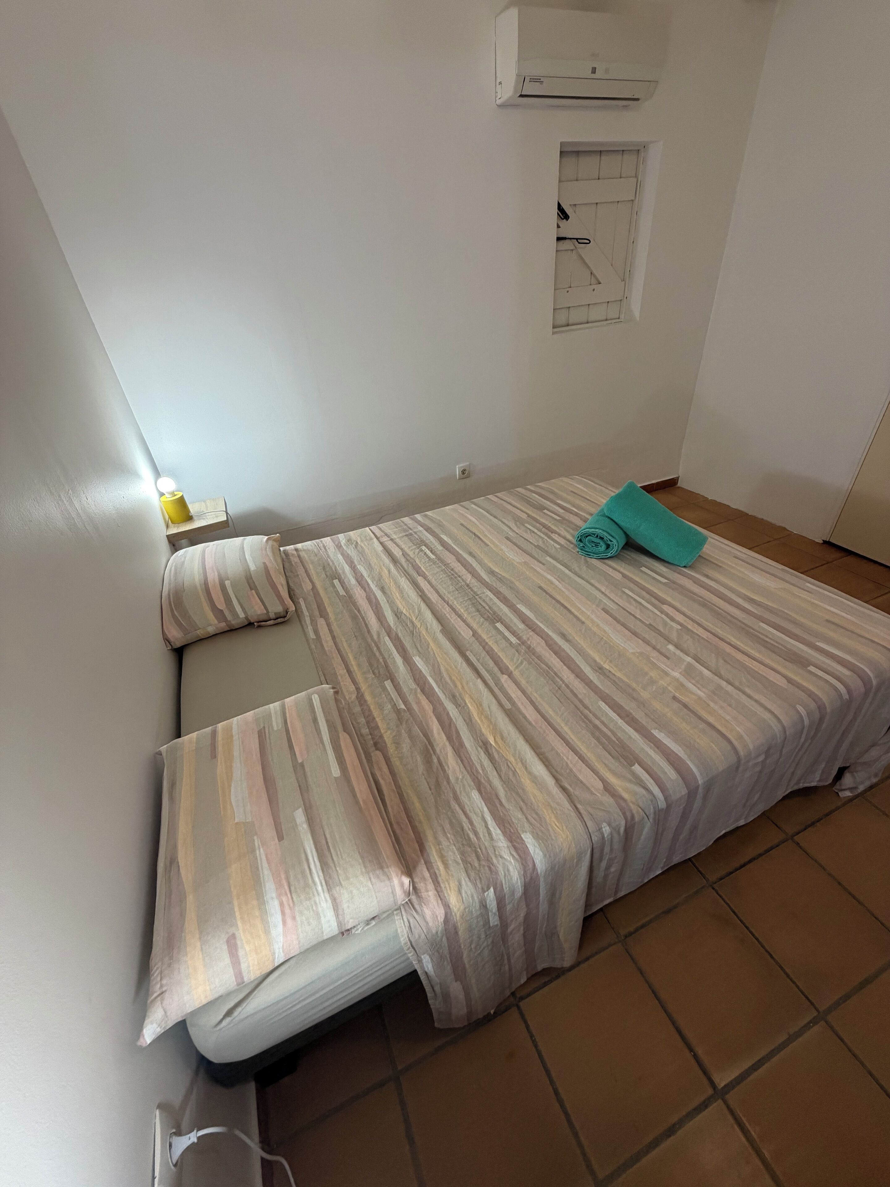 Een compact, verzorgd slaapkamer met een enkel bed, een nachtkastje met lamp en een airconditioner aan de muur.