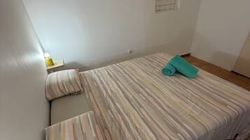 Een compact, verzorgd slaapkamer met een enkel bed, een nachtkastje met lamp en een airconditioner aan de muur.