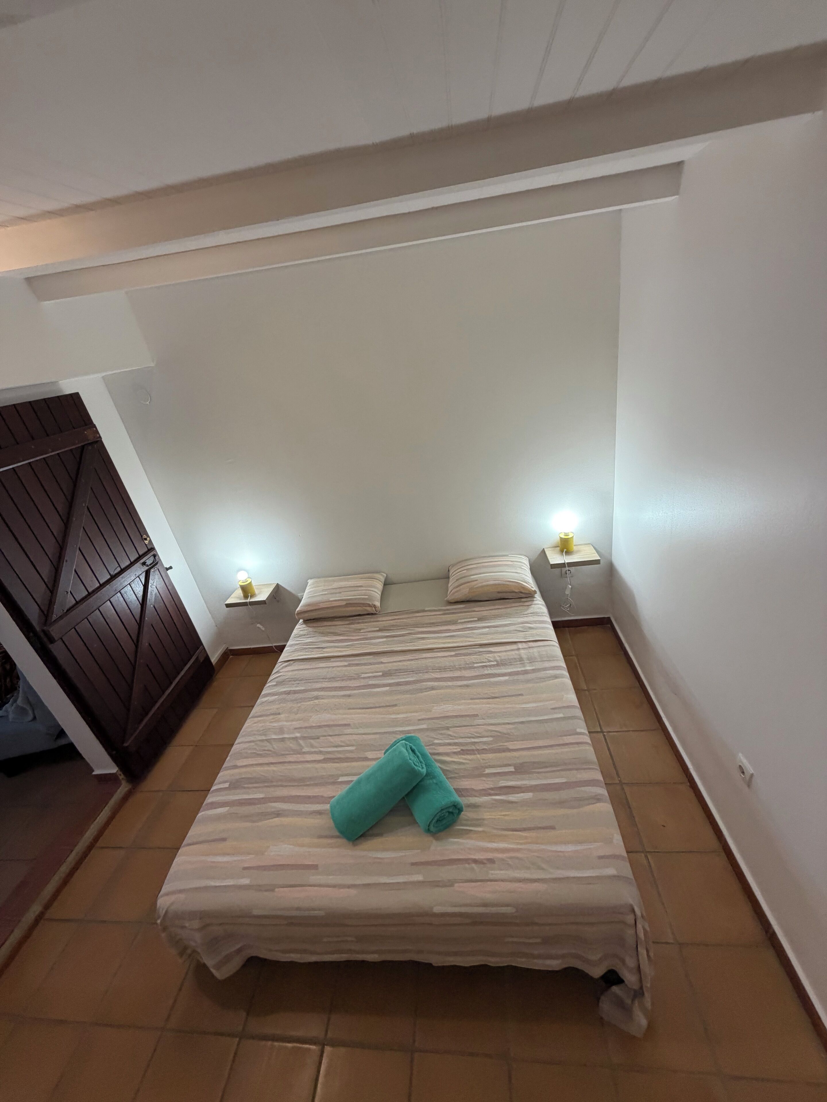 Ein Einzelbett mit gestreiftem Bettbezug und zwei Kissen, ein Nachttisch mit Lampe und eine Holztür.