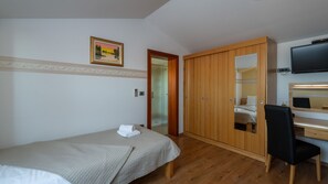 Ein Schlafzimmer mit Bett, Schreibtisch, Stuhl, Kleiderschrank, Fernseher und einem Bild an der Wand.