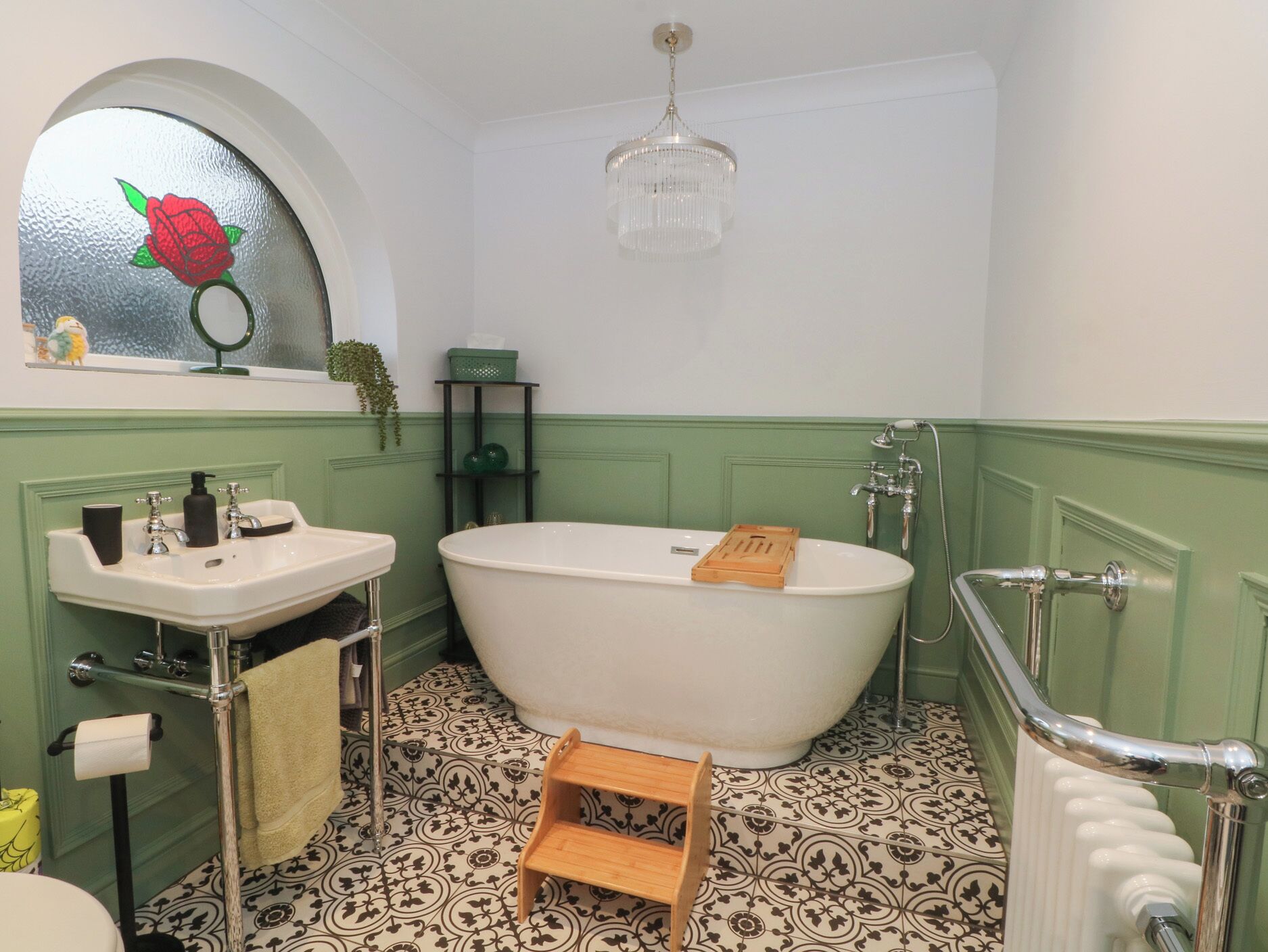 Un baño con una bañera independiente, un lavamanos con espejo y una pared verde.