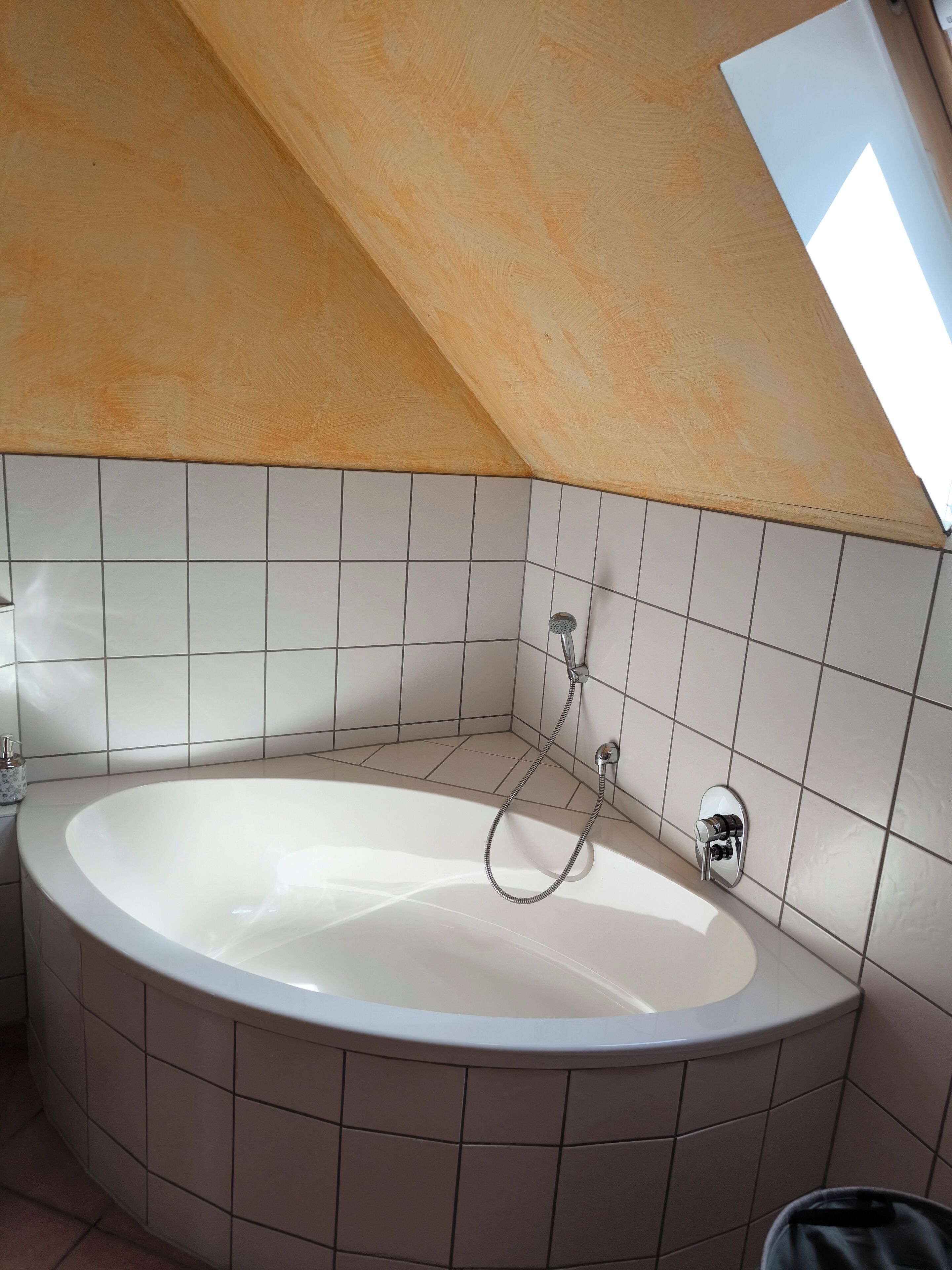 A modern bathroom with a freestanding bathtub, tiled walls, and a sloped ceiling.