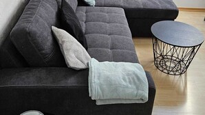 A modern living room with a sectional sofa, a small round table, and a wall-mounted light fixture. - Spacious vacation apartment (90 sqm) to feel good on 2 levels with balcony (Michelstadt)
