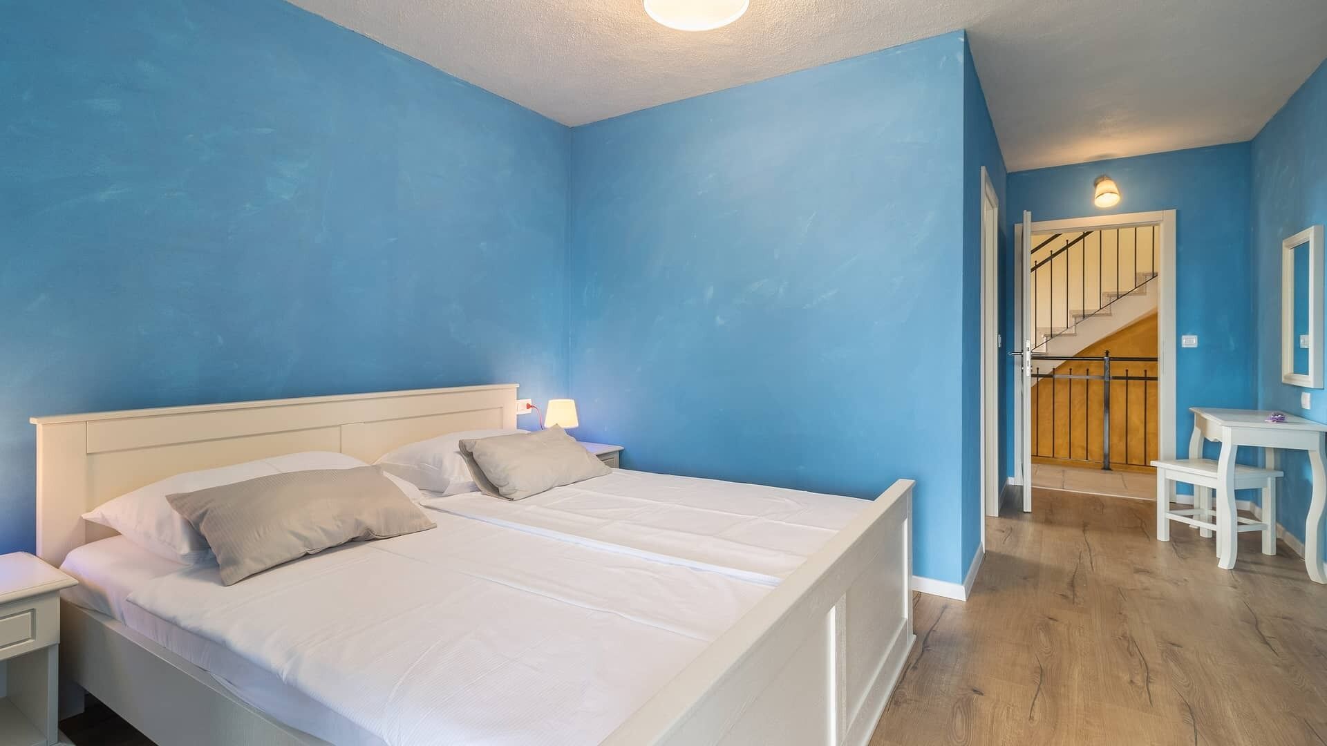 A bedroom with a white bed, two bedside tables, and a nightstand. There is a staircase leading to an upper floor.
