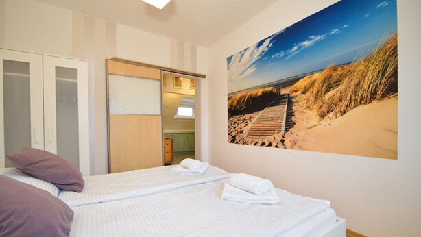 A hotel room with a bed, a wardrobe, a bathroom, and a beach view poster. - RentPlanet - Apartament Narutowicza (Kołobrzeg)