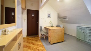 A small, well-lit room with a wooden desk, a chair, a small cabinet, and a mirror. There is a door with a sign on it, and a wall-mounted shelf with a vase. - RentPlanet - Apartament Narutowicza (Kołobrzeg)