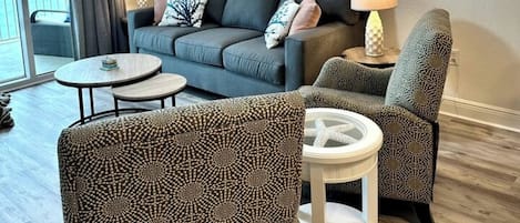 Una sala de estar moderna con un sofá gris, sillones estampados, una mesa de centro y un ventilador de techo.