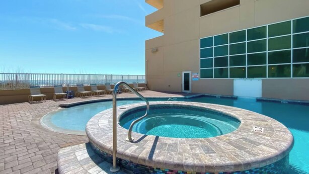 Una piscina en la azotea con borde de mosaico, sillas de descanso y vista despejada del horizonte de la ciudad.