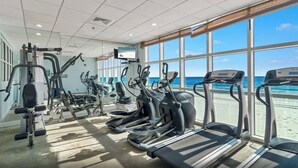 Un gimnasio con cintas de correr, elípticas y equipo de pesas, con vistas a una playa.