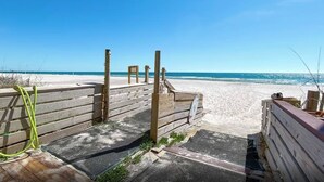 Una entrada de madera a la playa con un sendero arenoso que lleva al mar.