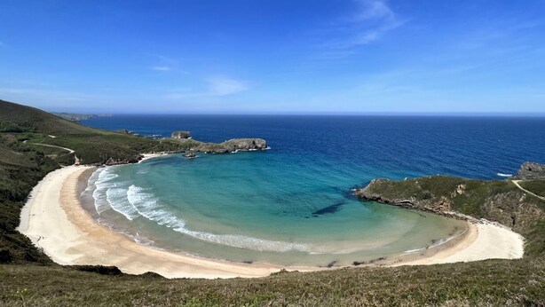 A coastal landscape with a curved sandy beach, clear blue sea, and rocky outcrops. - VILLA WITH LAND IN LLANES (La Pereda)