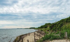 A sandy beach with a wooden fence and greenery. - 5 Person Holiday Home in Roslev (Roslev)