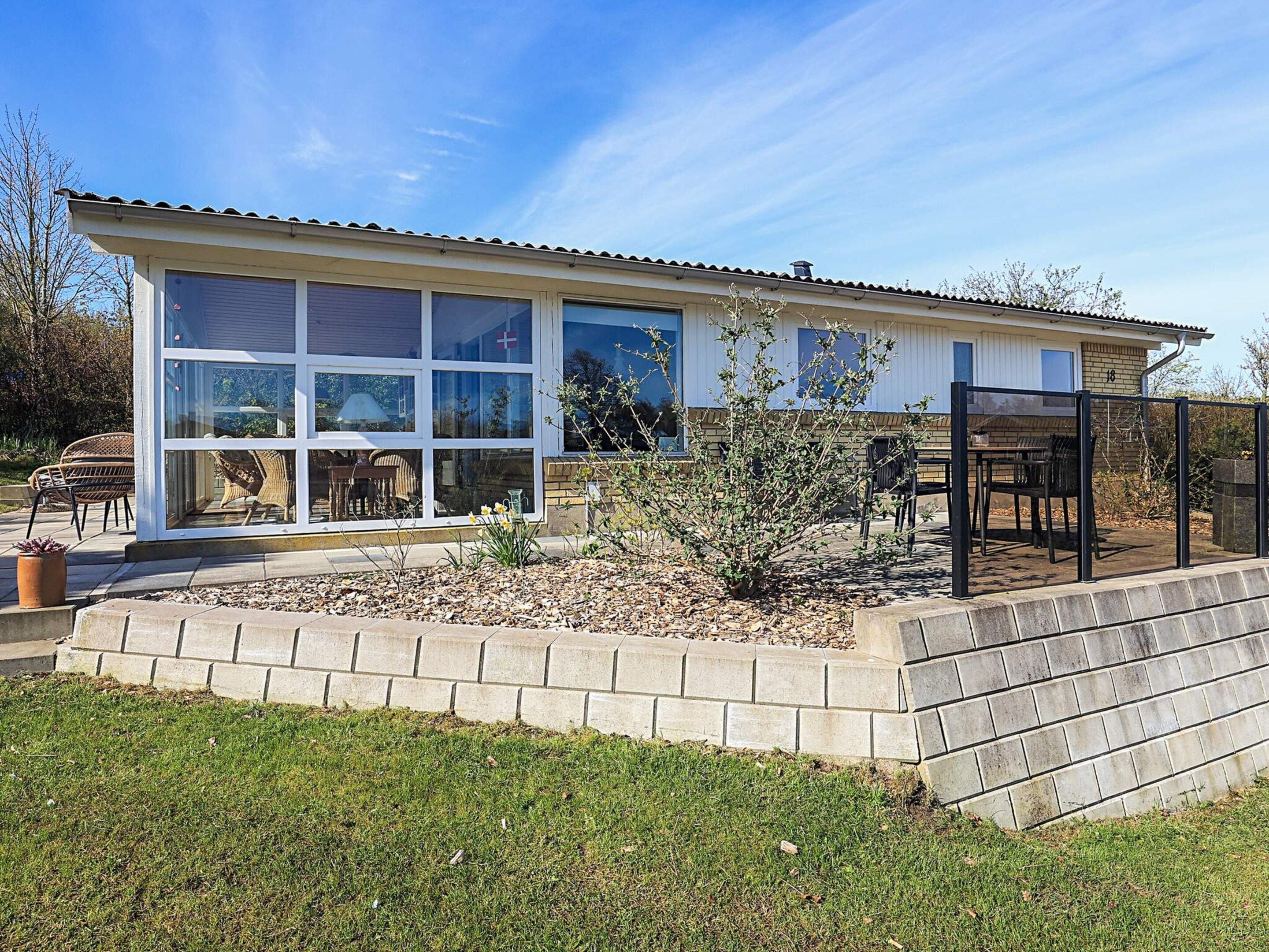 A modern house with large windows, a patio with outdoor furniture, and a well-maintained garden.