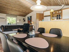 A modern dining area with a wooden ceiling, a black dining table with pink placemats, black chairs, and a wooden counter with shelves. - 5 Person Holiday Home in Roslev (Roslev)