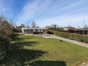 A residential area with a house featuring a large glass window section, a well-maintained lawn, and a gravel driveway. - 5 Person Holiday Home in Roslev (Roslev)