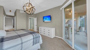 Ein Schlafzimmer mit einem Bett, einem Fernseher, einem Schminktisch und einer Glasgleittür, die auf einen Balkon führt.