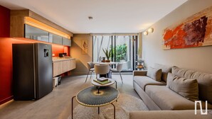 A modern living room with a sofa, a dining table with chairs, a kitchen area with a refrigerator, and a large window with curtains. - NOK Spacious 3BR Apartment Near Zona T Bogota (Bogotá)