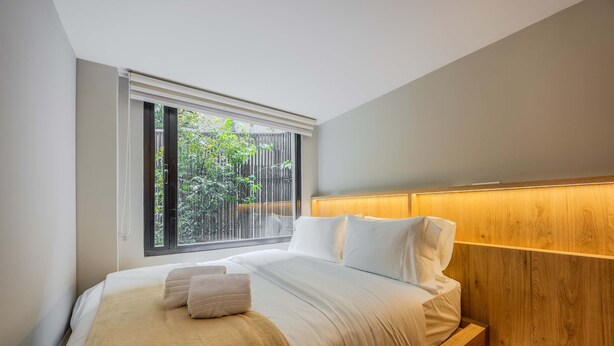 A modern bedroom with a large window, a wooden headboard, and a neatly made bed with white linens and a beige throw blanket. - NOK Spacious 3BR Apartment Near Zona T Bogota (Bogotá)