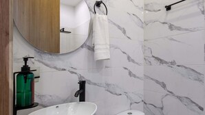 A bathroom with a marble wall, a round mirror, a white sink, and a toilet. - NOK Stylish 1-bedroom With Terrace on Calle 94 (Bogotá)