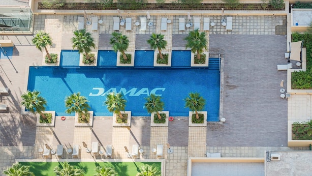 Vista aérea de un área de piscina con la marca 'DAMAC', rodeada de tumbonas y palmeras.