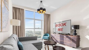 Una sala de estar moderna con un sofá, un televisor, una silla azul y vistas a un paisaje urbano a través de amplios ventanales.