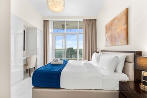 A modern hotel room with a large bed, a desk, and a view of the city through large windows. - Stayshort - 1BR in JVC That Sleeps 4 With Amazing Amenities (Dubai)