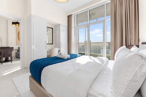 A hotel room with a large bed, a desk, and a window with curtains. - Stayshort - 1BR in JVC That Sleeps 4 With Amazing Amenities (Dubai)