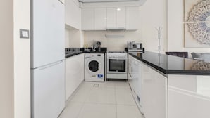 Una cocina moderna con armarios blancos, lavadora integrada, horno y encimera de vidrio.