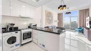 Cocina moderna con lavavajillas, horno y lavadora. Cuenta con un comedor, una silla azul y vistas a la ciudad.