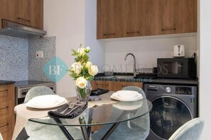 A modern kitchen with wooden cabinets, a glass dining table, and a washing machine. - Bloomfields Stylish 1BR In Oasis Mas (Abu Dhabi)