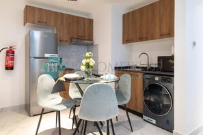 Eine moderne Küche mit Holzausstattung, einem Edelstahlkühlschrank, einer Waschmaschine und einem Essbereich mit Glastisch und grauen Stühlen.