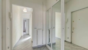 En hall med en glasdörr som leder in till ett rum, en lampa i taket och ett klinkergolv.